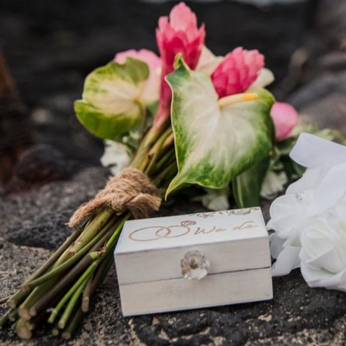 Couple holding hands at outdoor wedding ceremony on rocks near water.