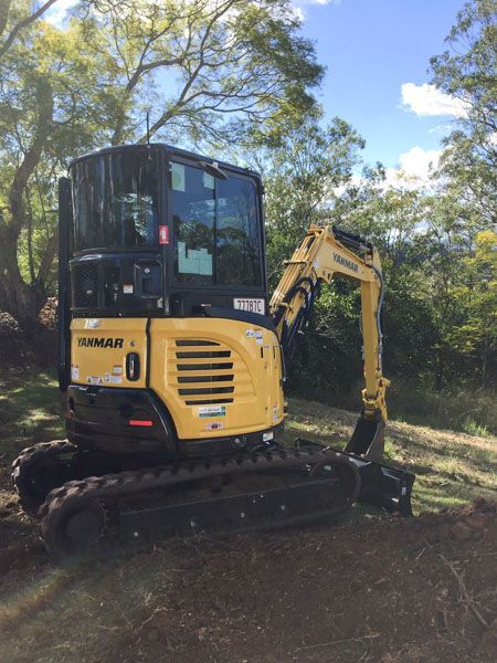 A small yellow excavator is parked in the middle of a field.