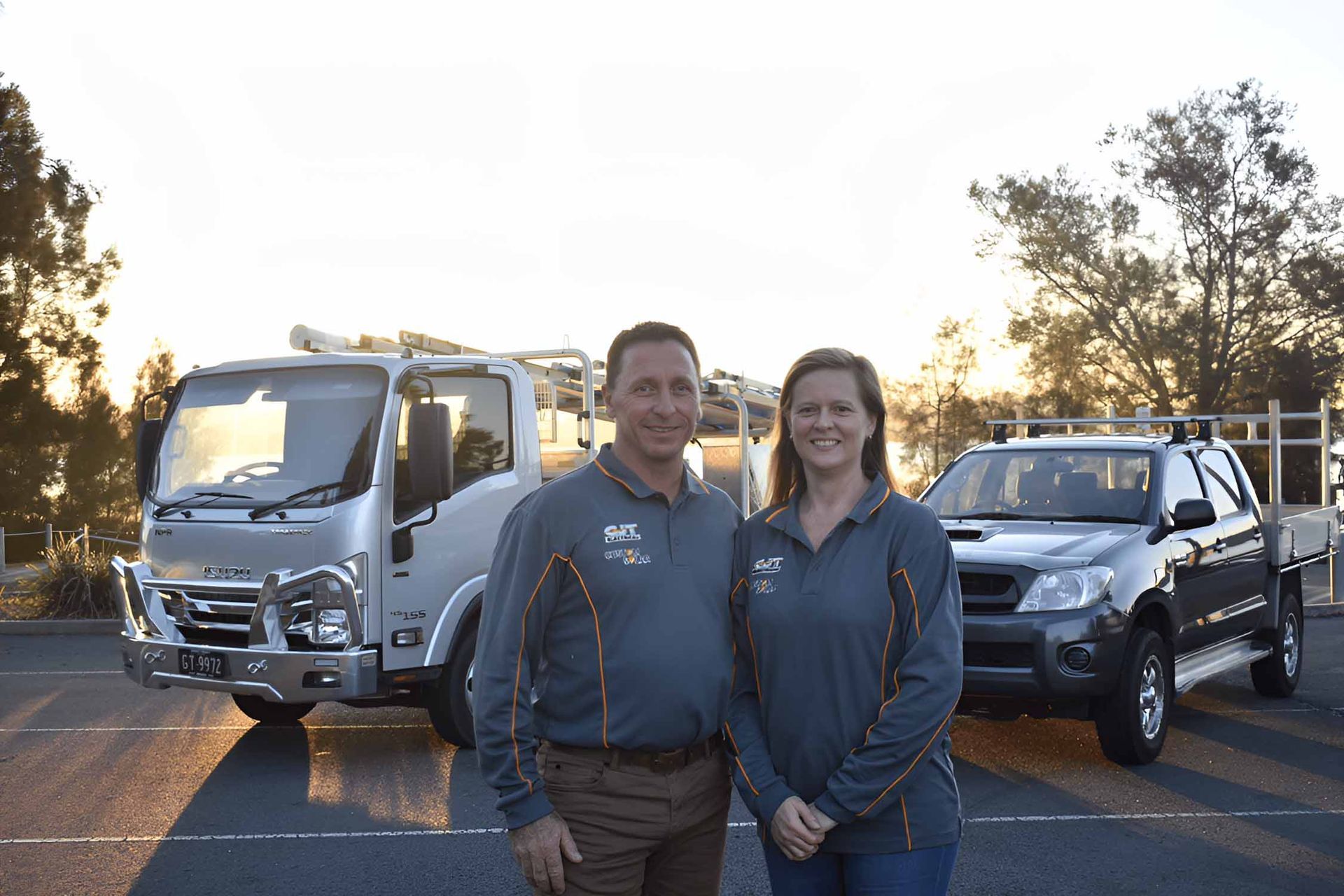 A Man And A Woman Are Standing In Front Of A Truck And A Truck — GJT Electrical In Warners Bay, NSW