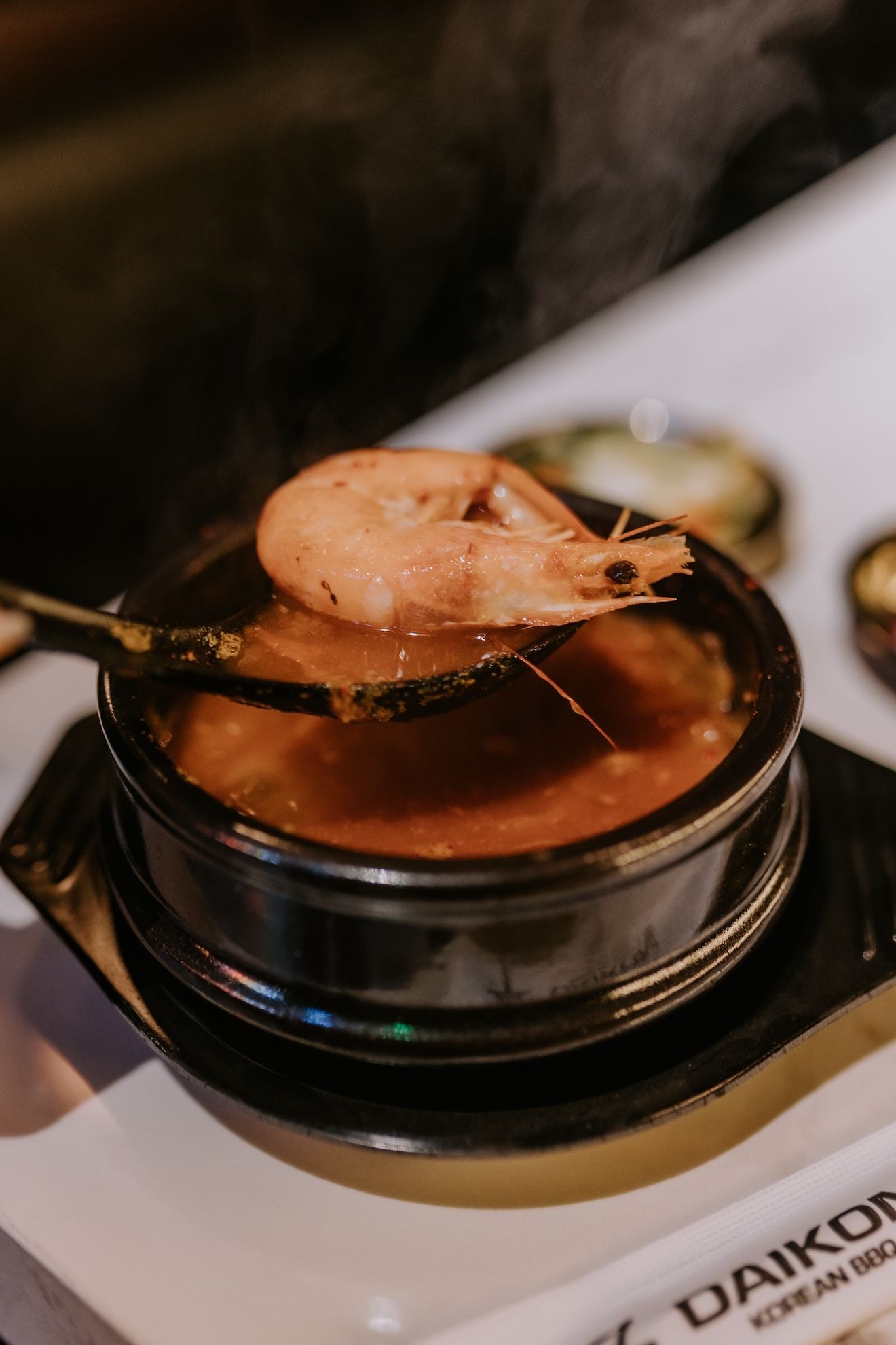 a shrimp is being scooped out of a bowl of soup with a spoon .