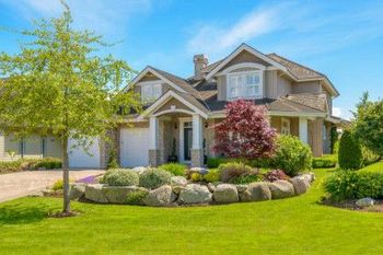 Suburban house with a green lawn, flower beds, and a tree in the front yard