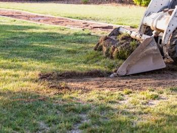 Backhoe bucket digging a dirt patch on a grassy field