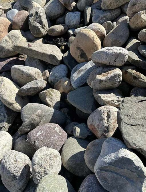Piles of rounded gray and tan rocks stacked outdoors in sunlight