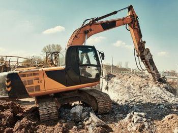 Orange excavator demolishing rubble at a construction site under a clear sky