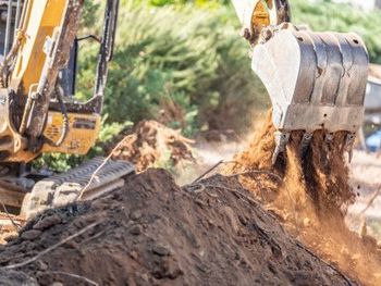 Excavator dumping dirt at a construction site, with soil spilling from the bucket.