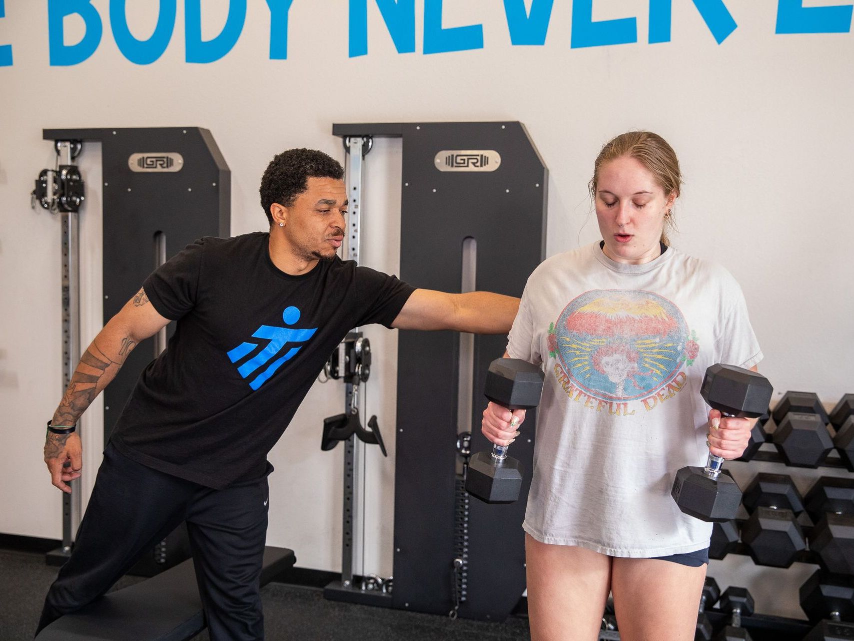 Trainer spotting a woman doing dumbbell raises in a gym