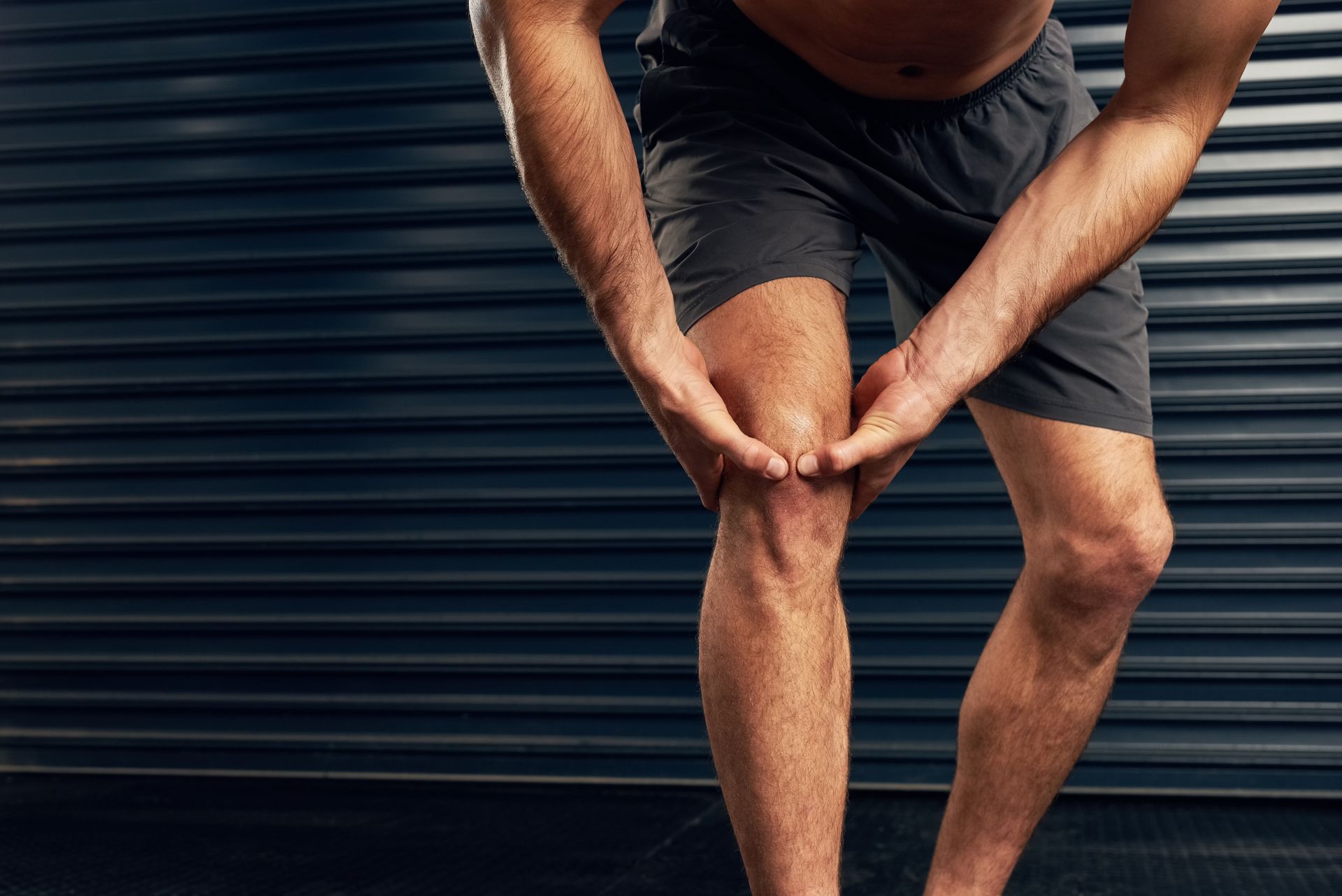 Man holding his knee, possibly in pain with acl tear, against a dark background.