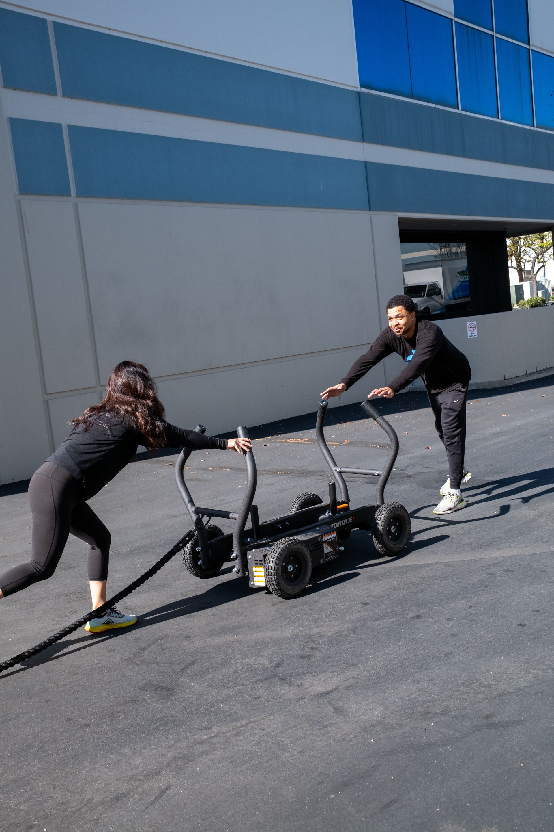 A man and a woman are pulling a cart with a rope.