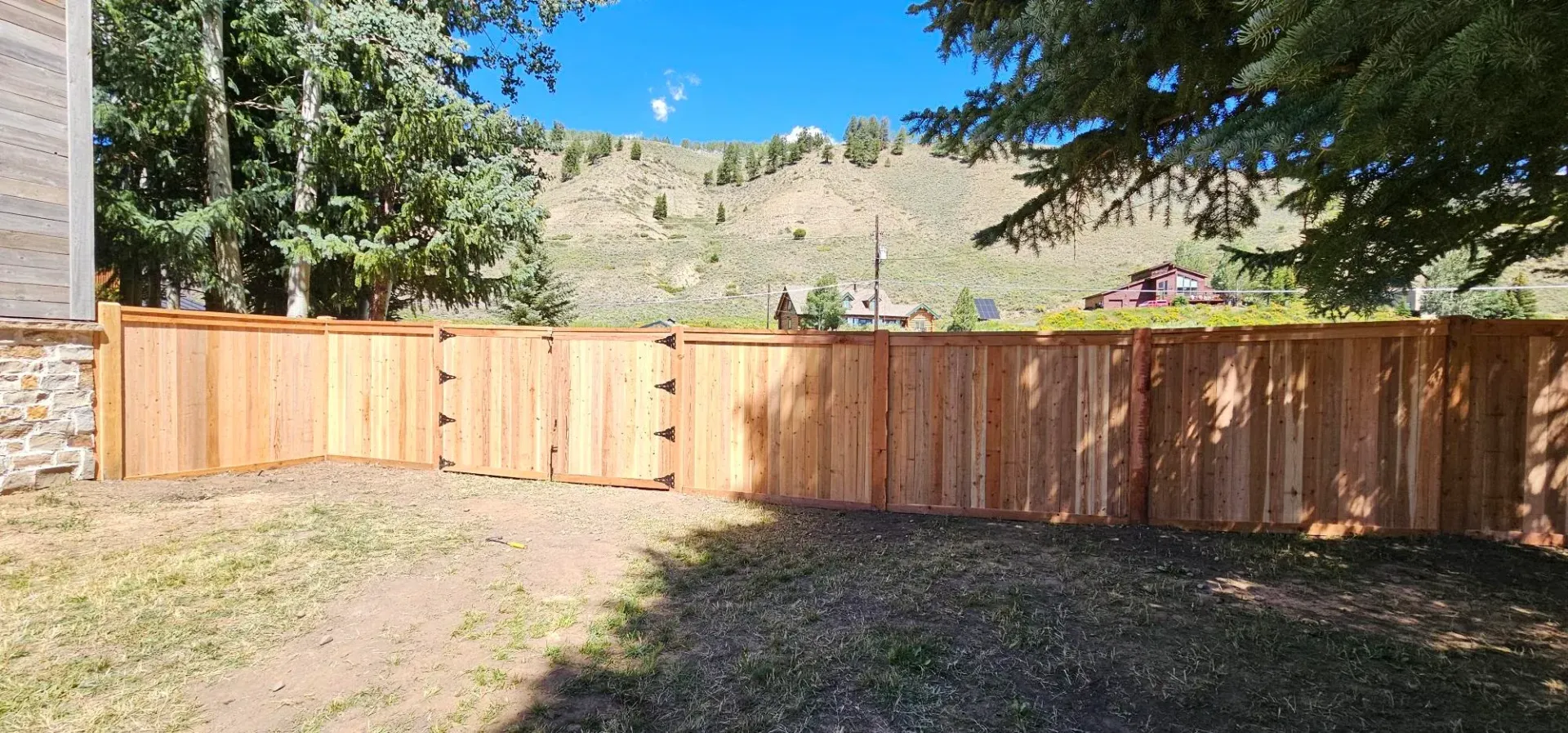 Wooden fence in a sunlit backyard with trees and hills beyond