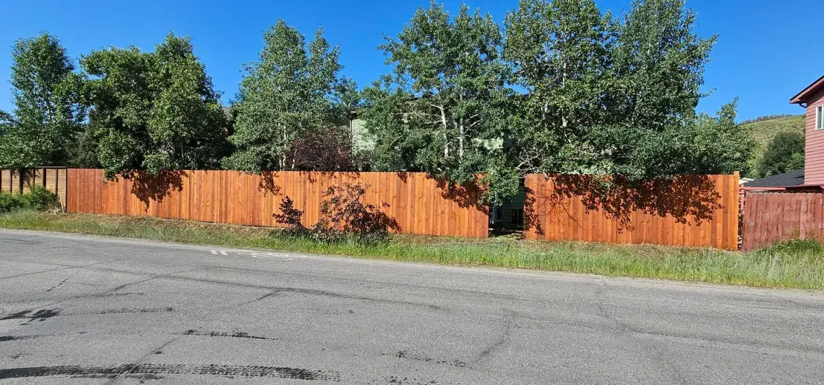 Orange fence along a quiet residential street with trees behind it under a clear blue sky
