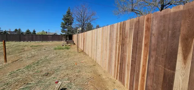 Long wooden fence along a dirt path under a clear blue sky in a backyard.