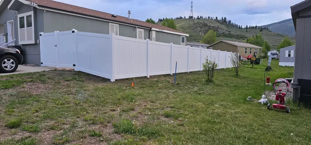 Row of white storage sheds beside a house on a grassy slope, with mountains in the background