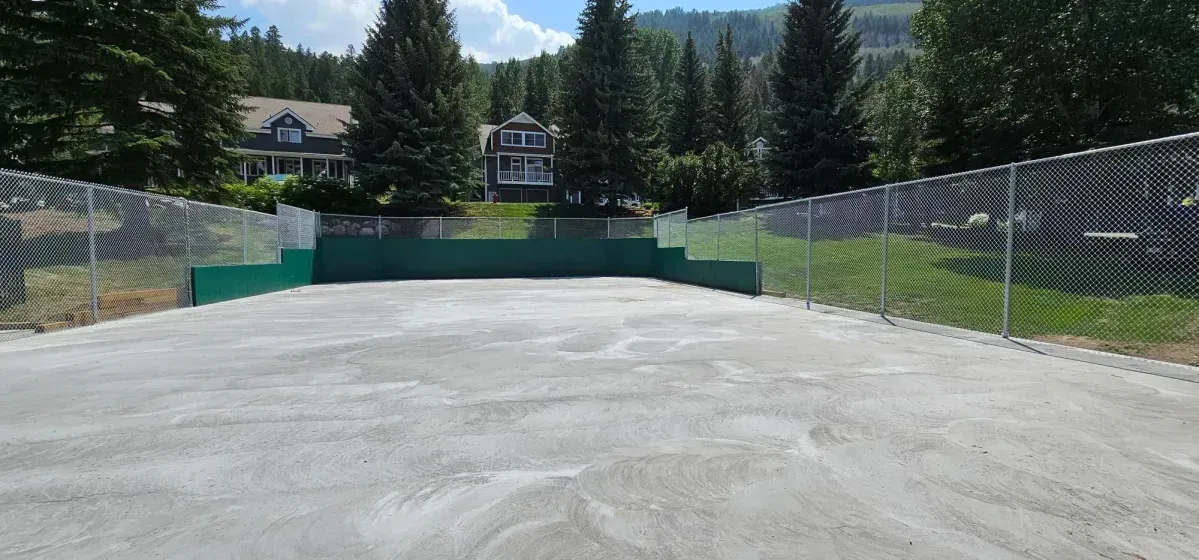 Empty concrete sports court with chain-link fencing, trees, and mountains in the background