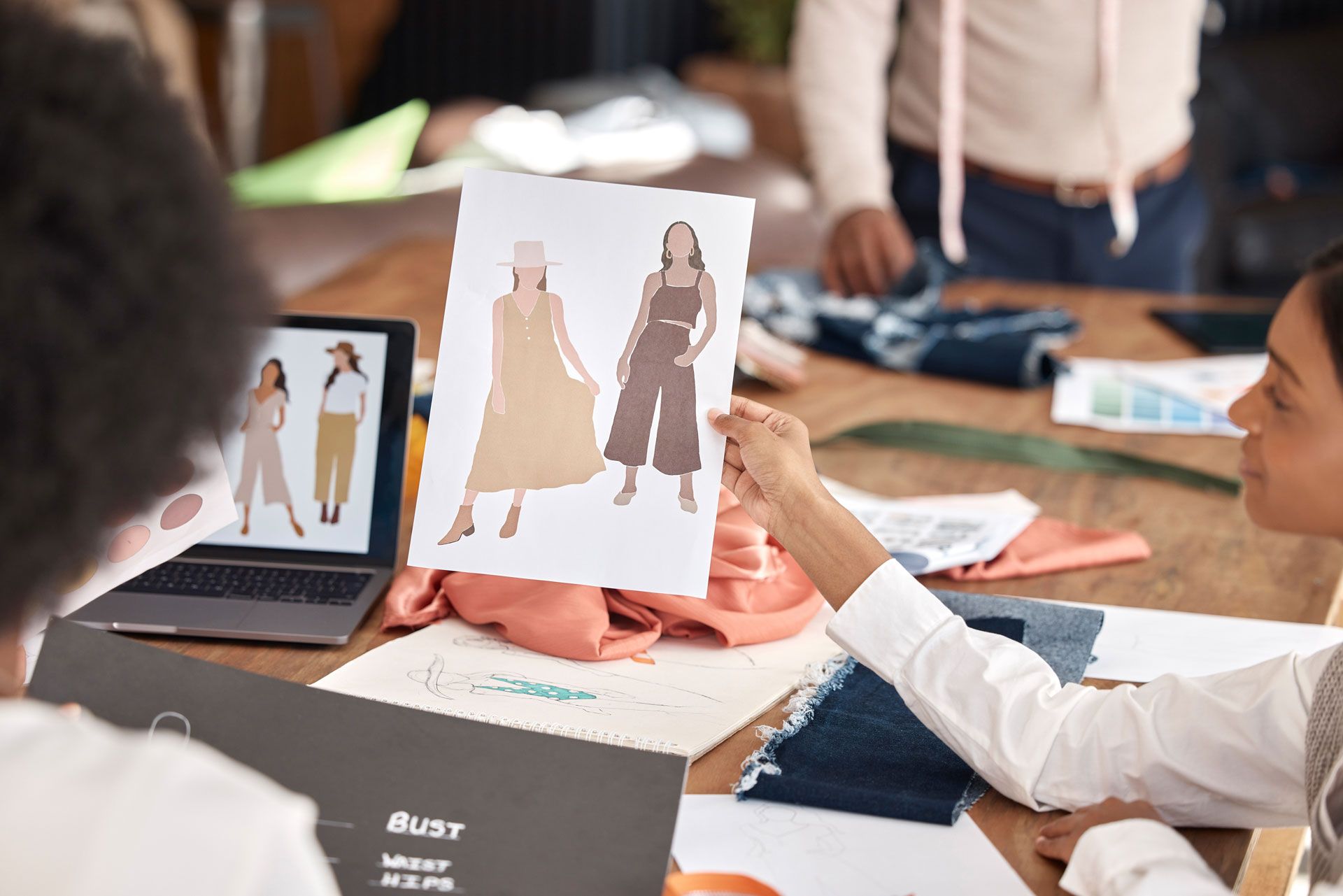 Designers reviewing clothing sketches and fabric swatches at a table in a workspace.