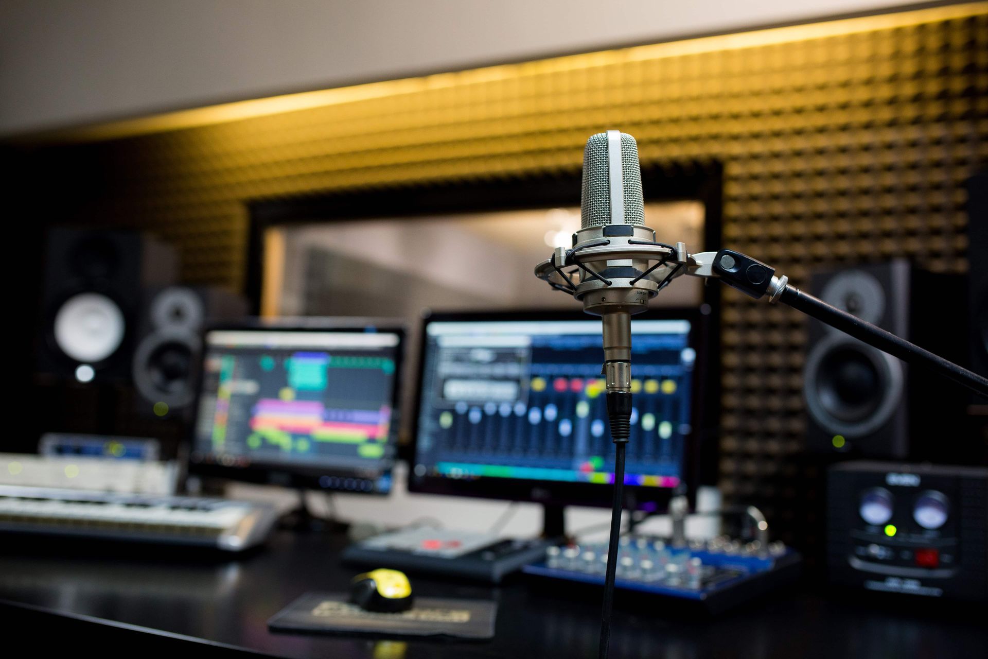 Studio setup with a microphone in focus, computer screens displaying audio editing software.