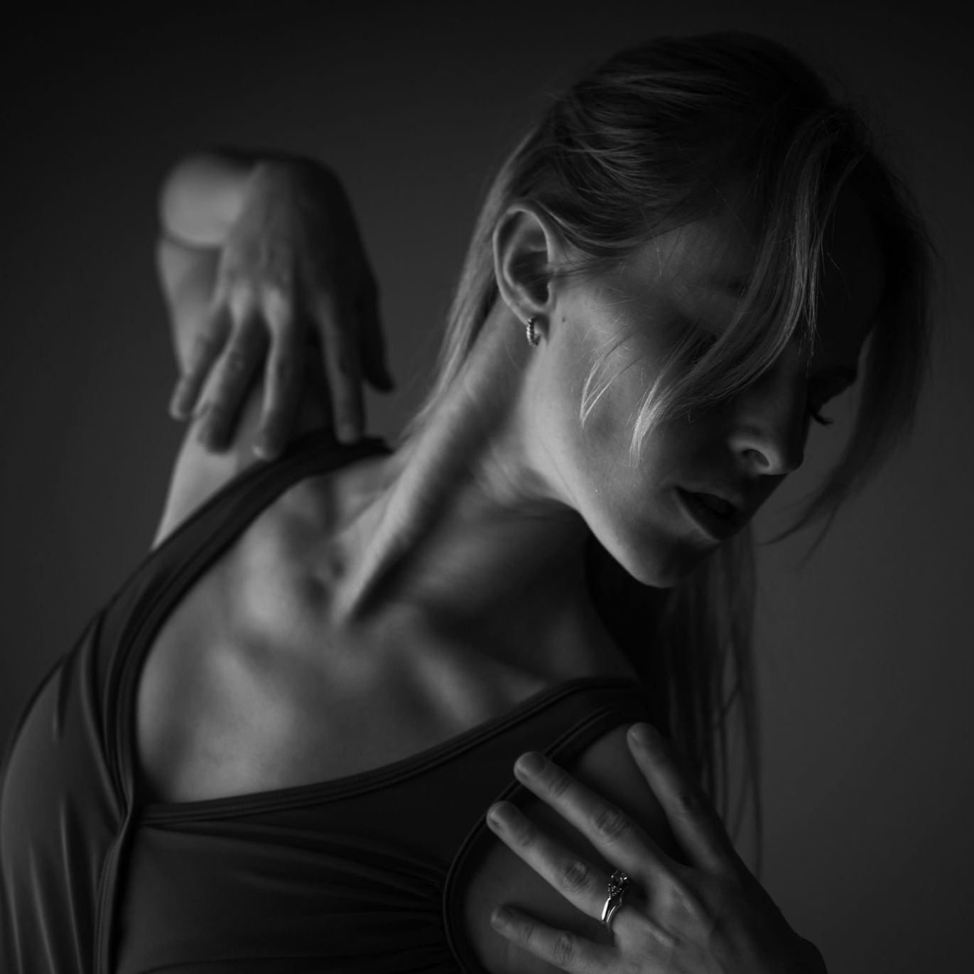 Black-and-white portrait of a person stretching a shoulder, with dramatic shadows and a dark background
