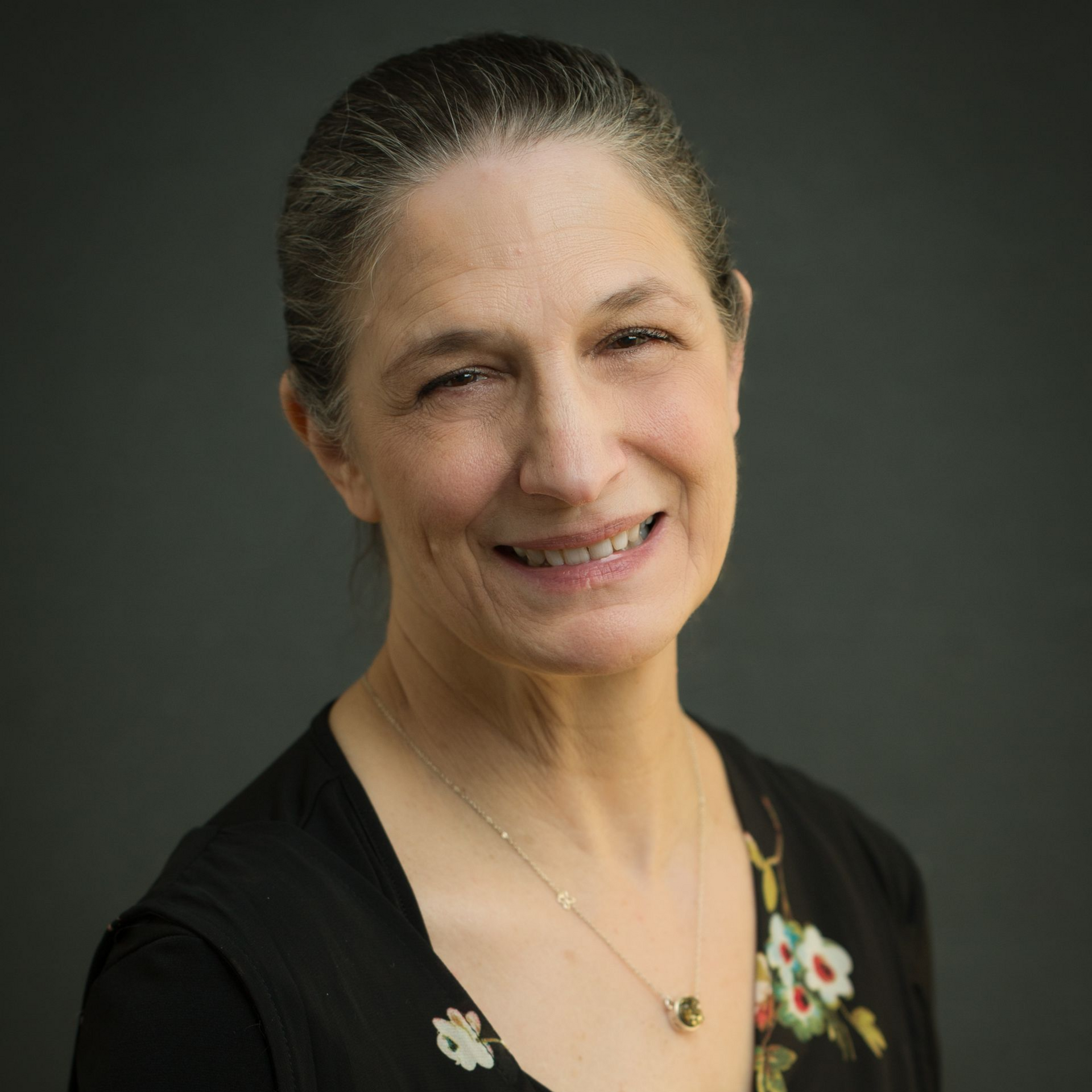 Smiling woman in a black floral top against a dark studio background
