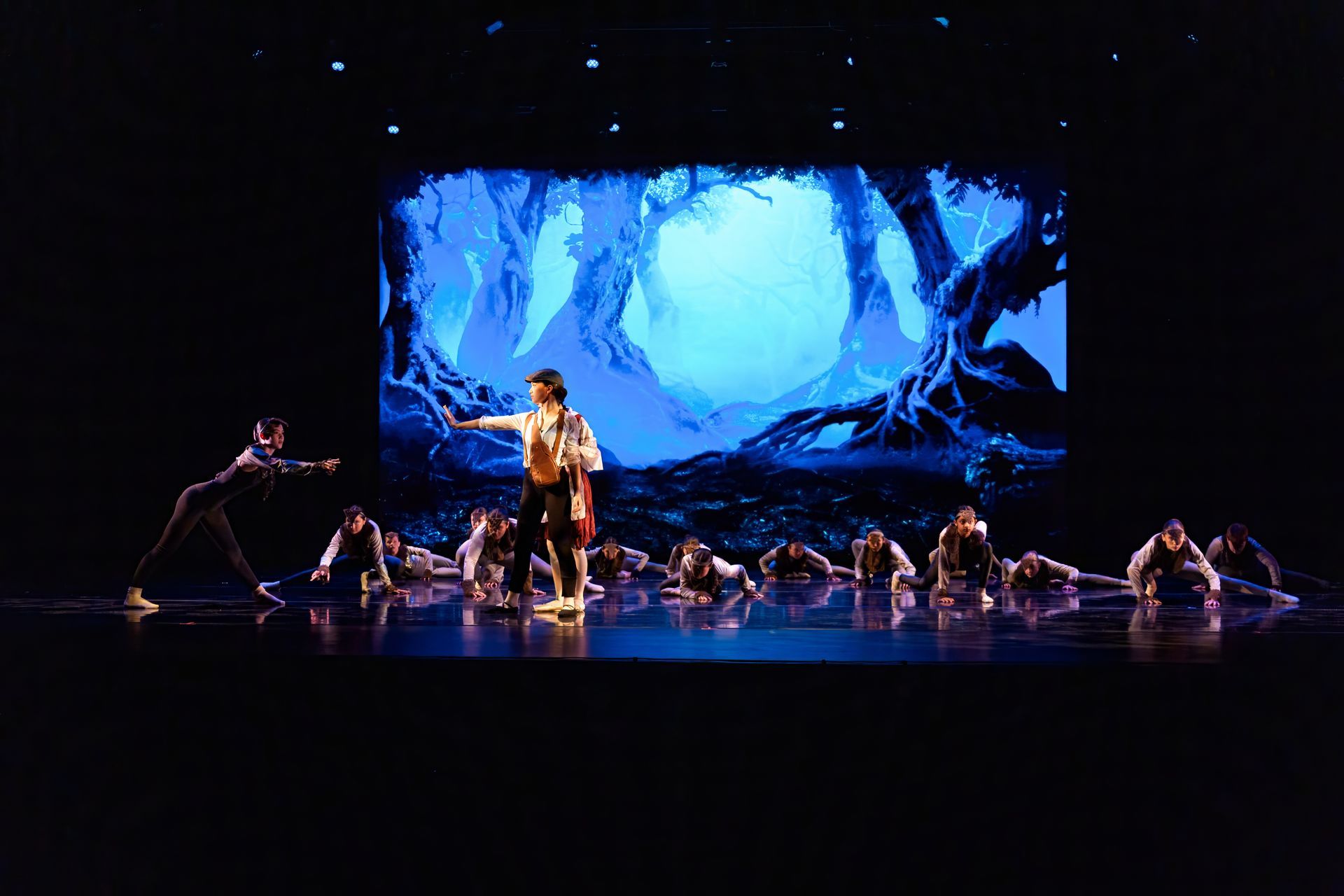 Dancers on a dark stage beneath a glowing blue forest backdrop