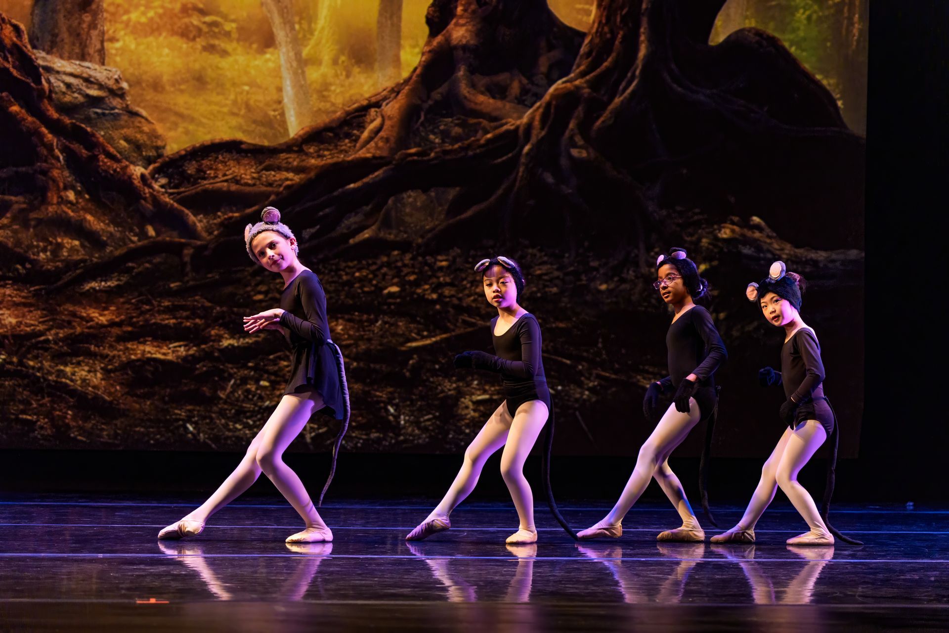 Four dancers in black costumes performing on a stage with a warm, rocky backdrop.