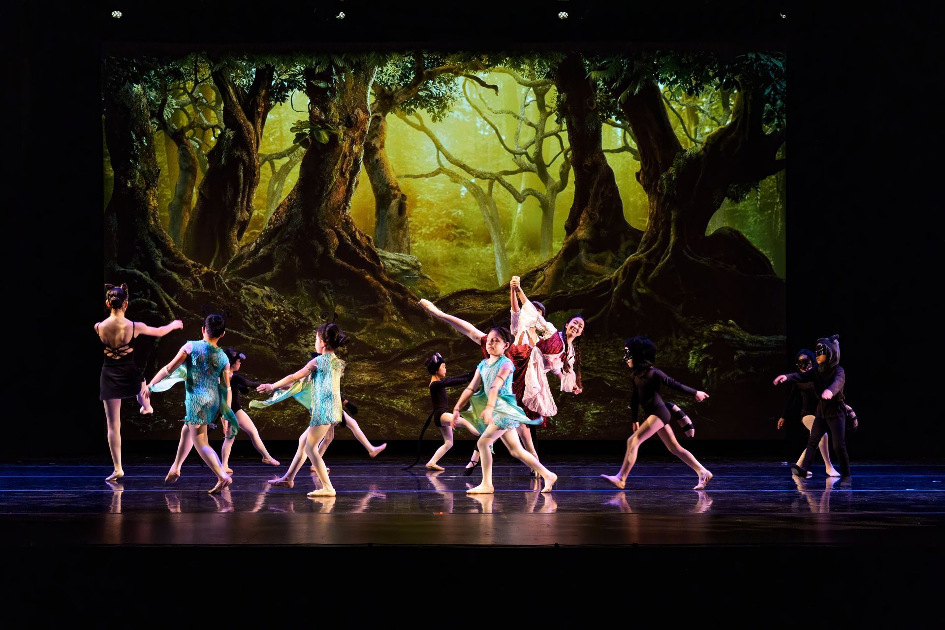 Dancers in pastel costumes perform onstage before a glowing forest backdrop