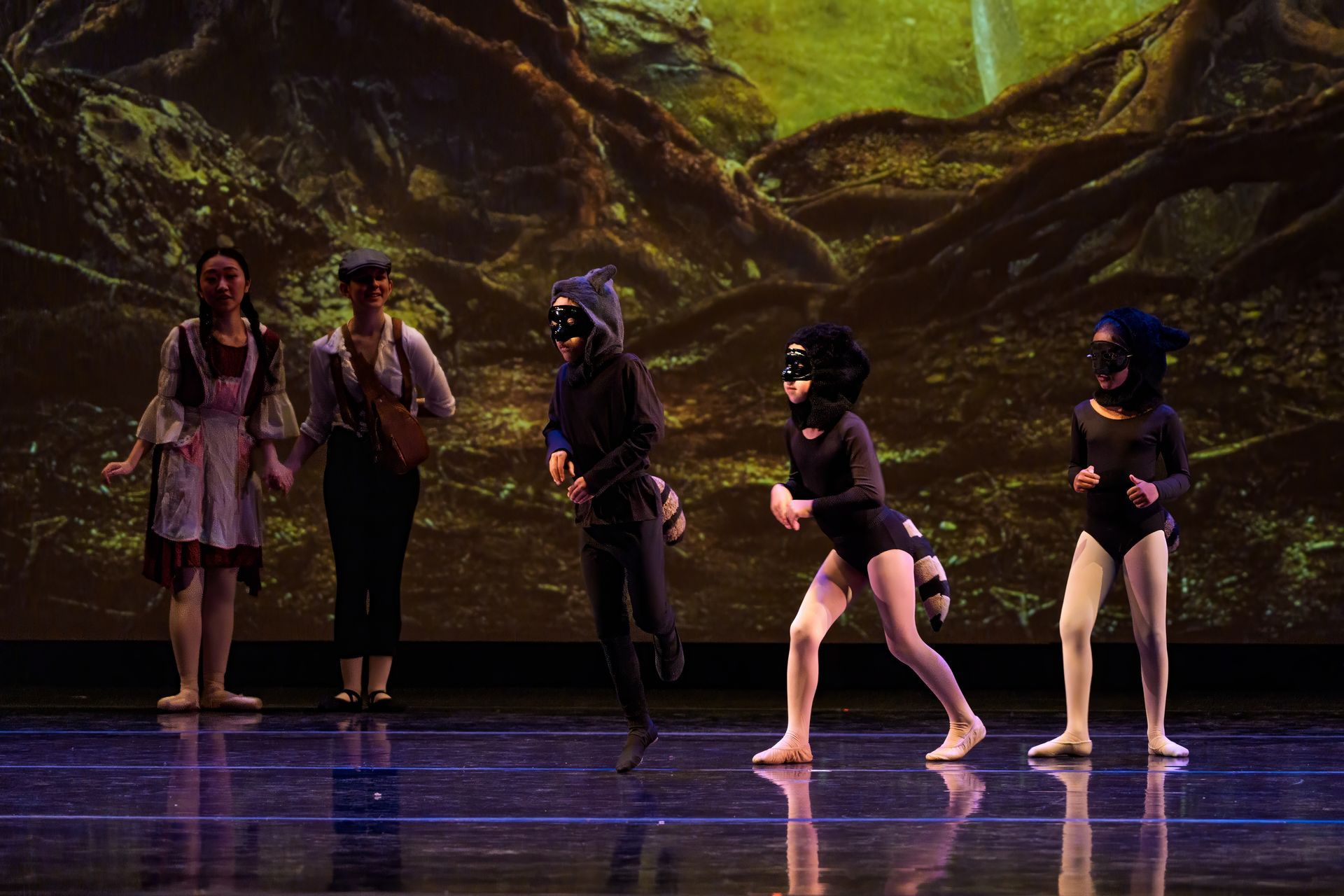 Five performers in dark costumes onstage, one crouching, under green and purple stage lighting