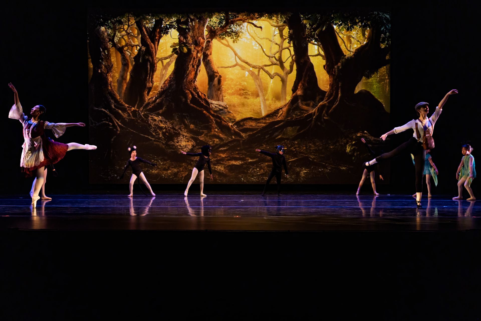 Ballet dancers on a stage with a glowing forest backdrop and warm golden lighting