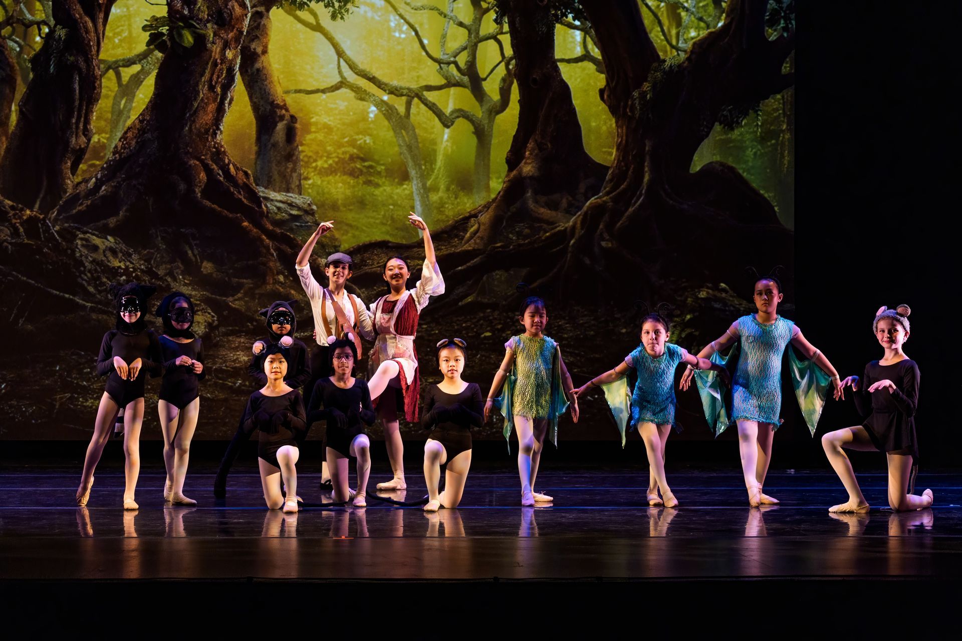 Dancers in colorful costumes performing on a stage with a forest backdrop