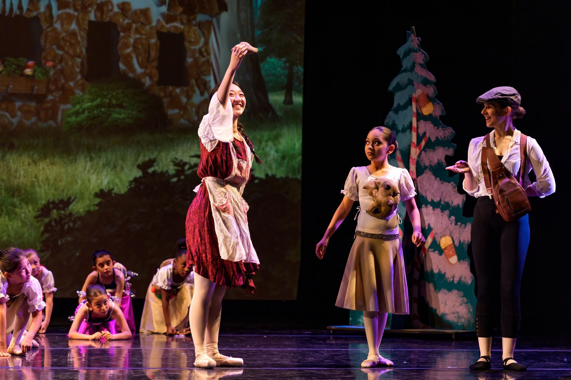 Performers in colorful costumes dancing on a theater stage with a forest backdrop