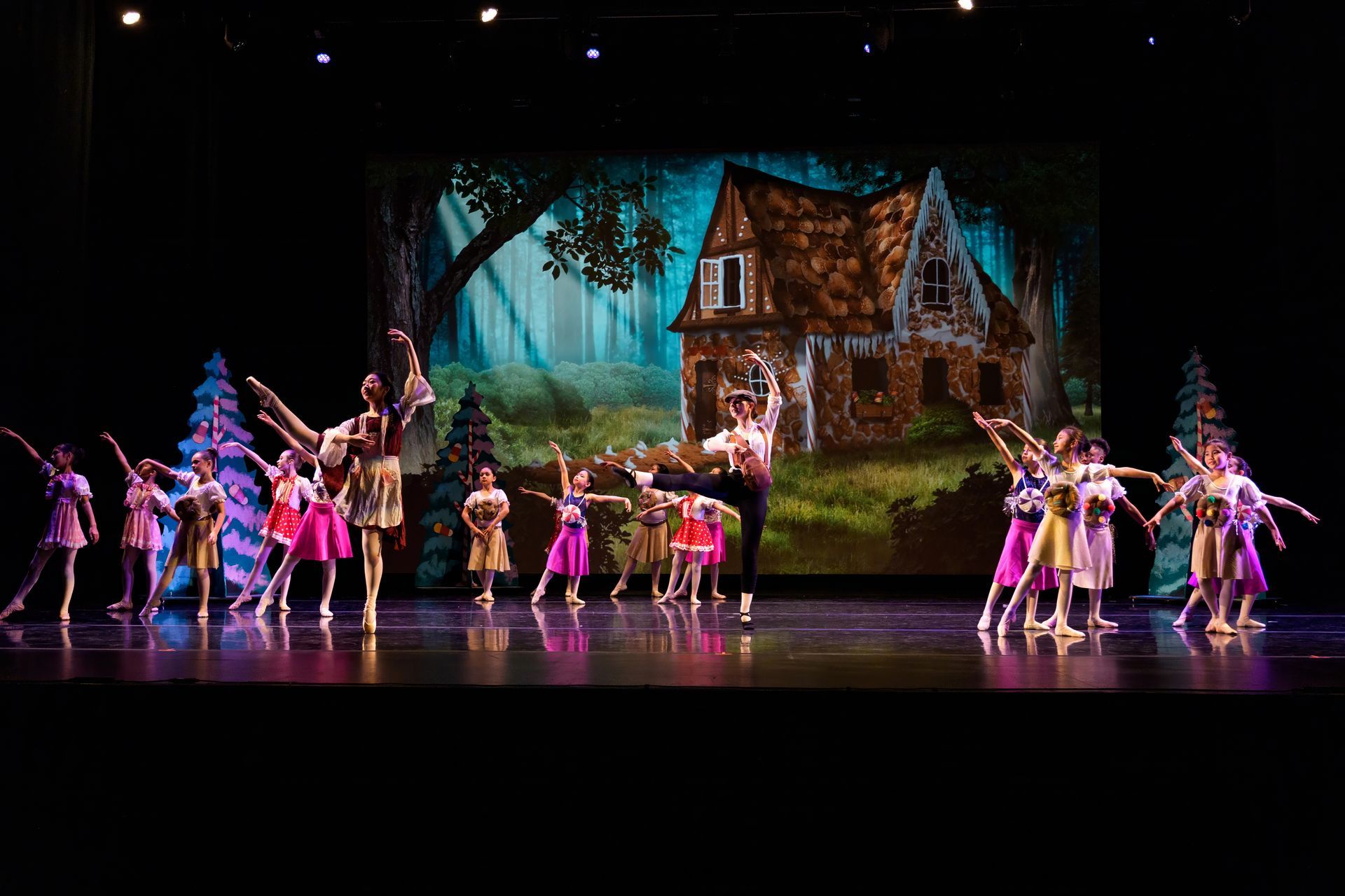 Dancers performing on a stage in front of a cottage backdrop, with colorful costumes and spotlights