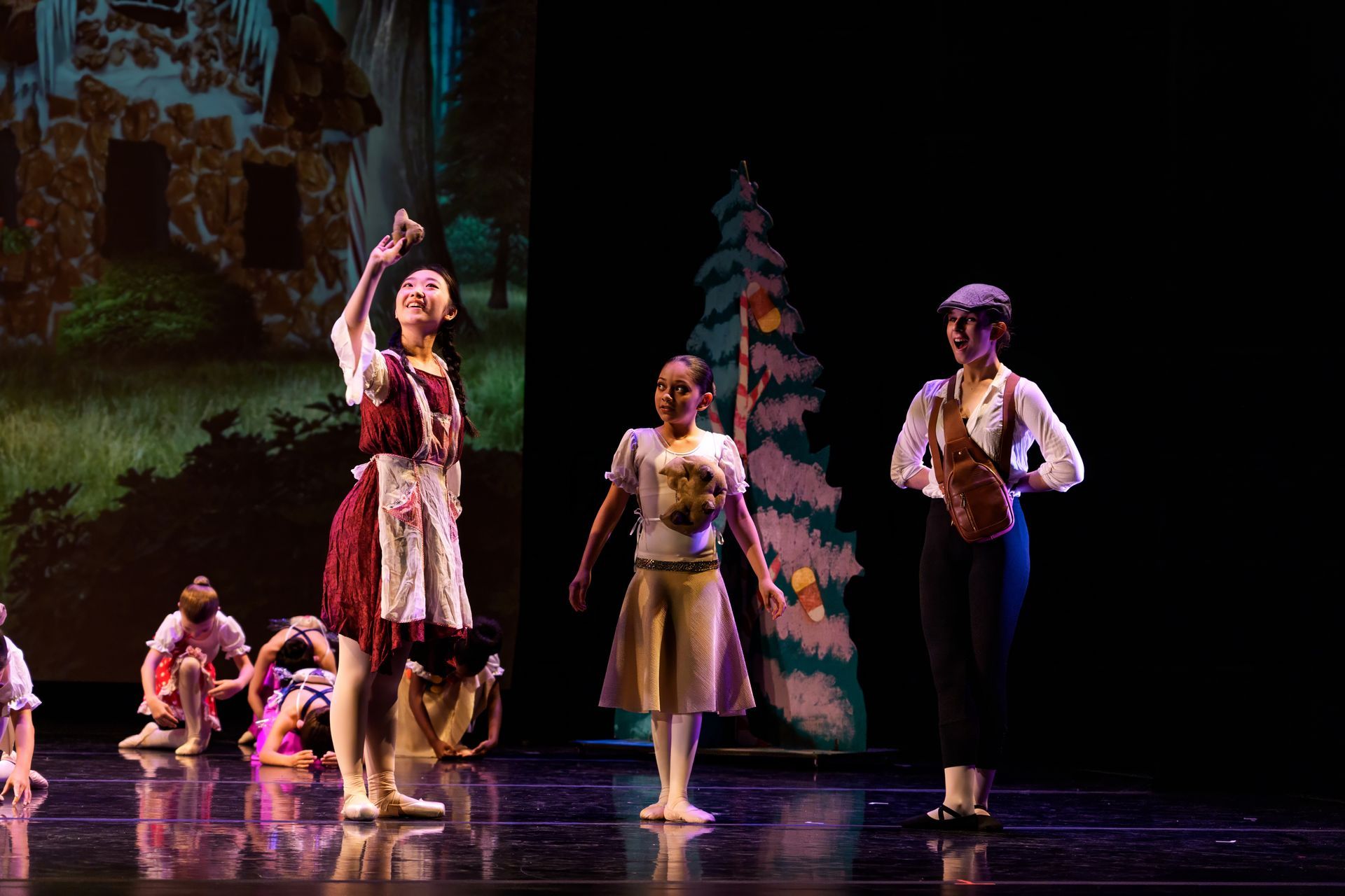 Children performing on a theater stage, with one girl raising an arm beside a boy and decorated backdrop.