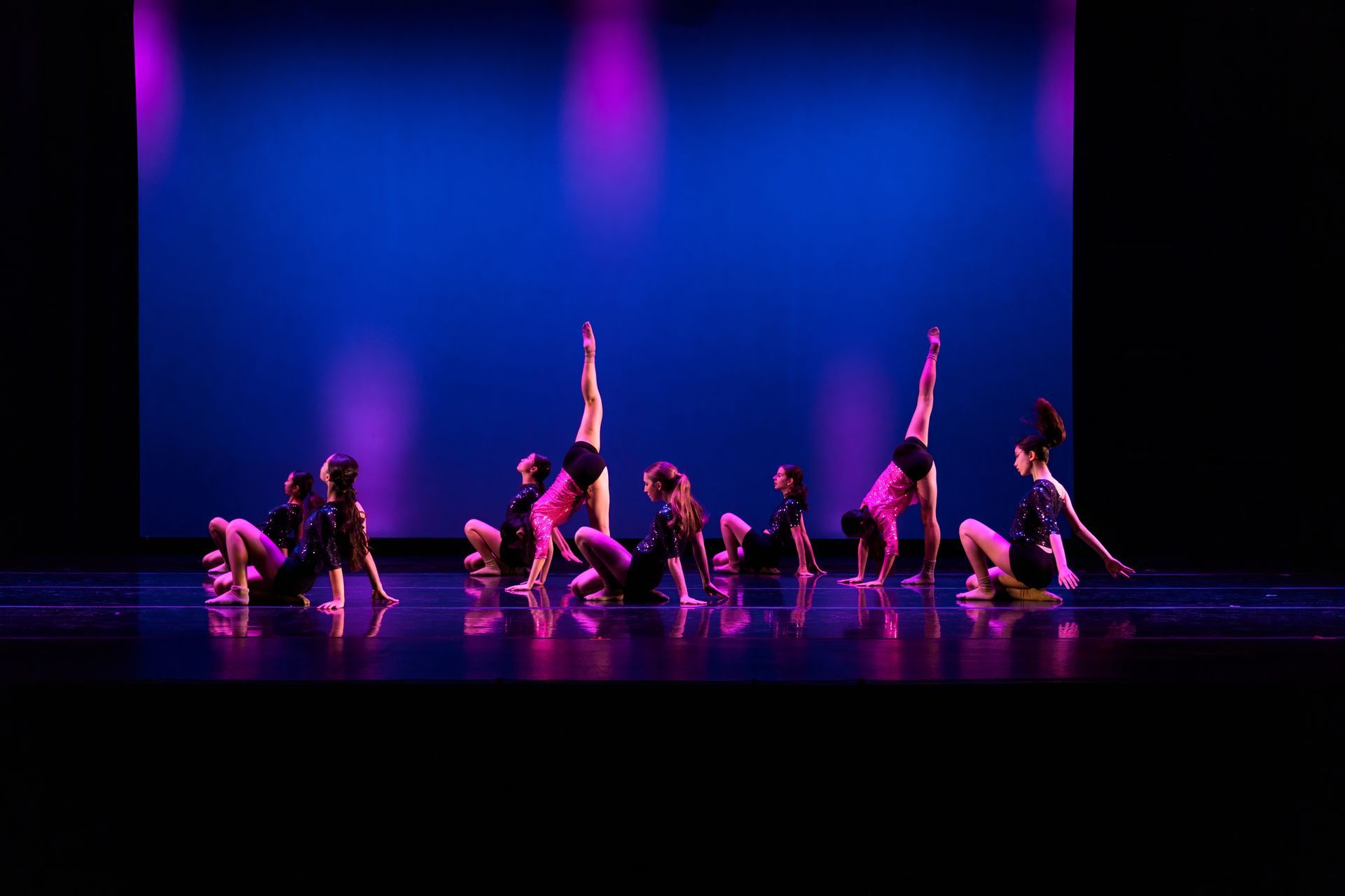 Dancers in pink costumes pose on a stage under blue and purple lights