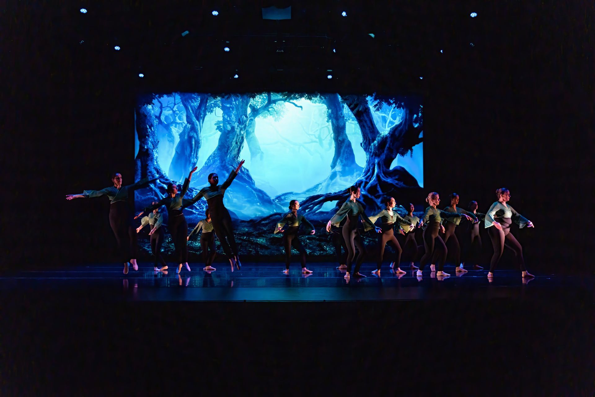 Dancers on a dark stage perform before a blue, icy digital backdrop