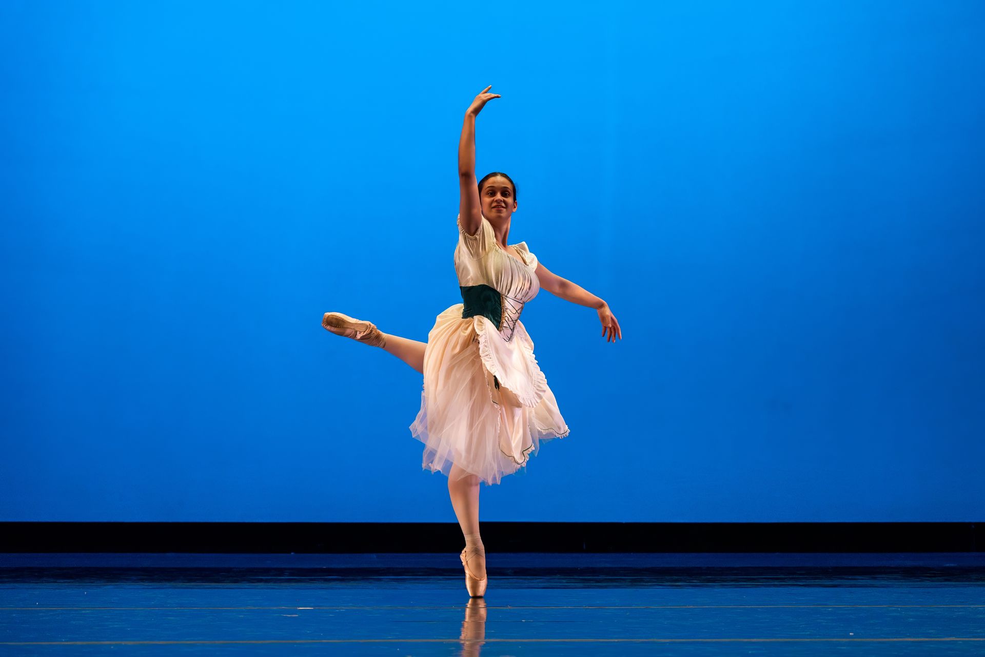 Ballet dancer in a pink tutu posing on stage against a blue backdrop