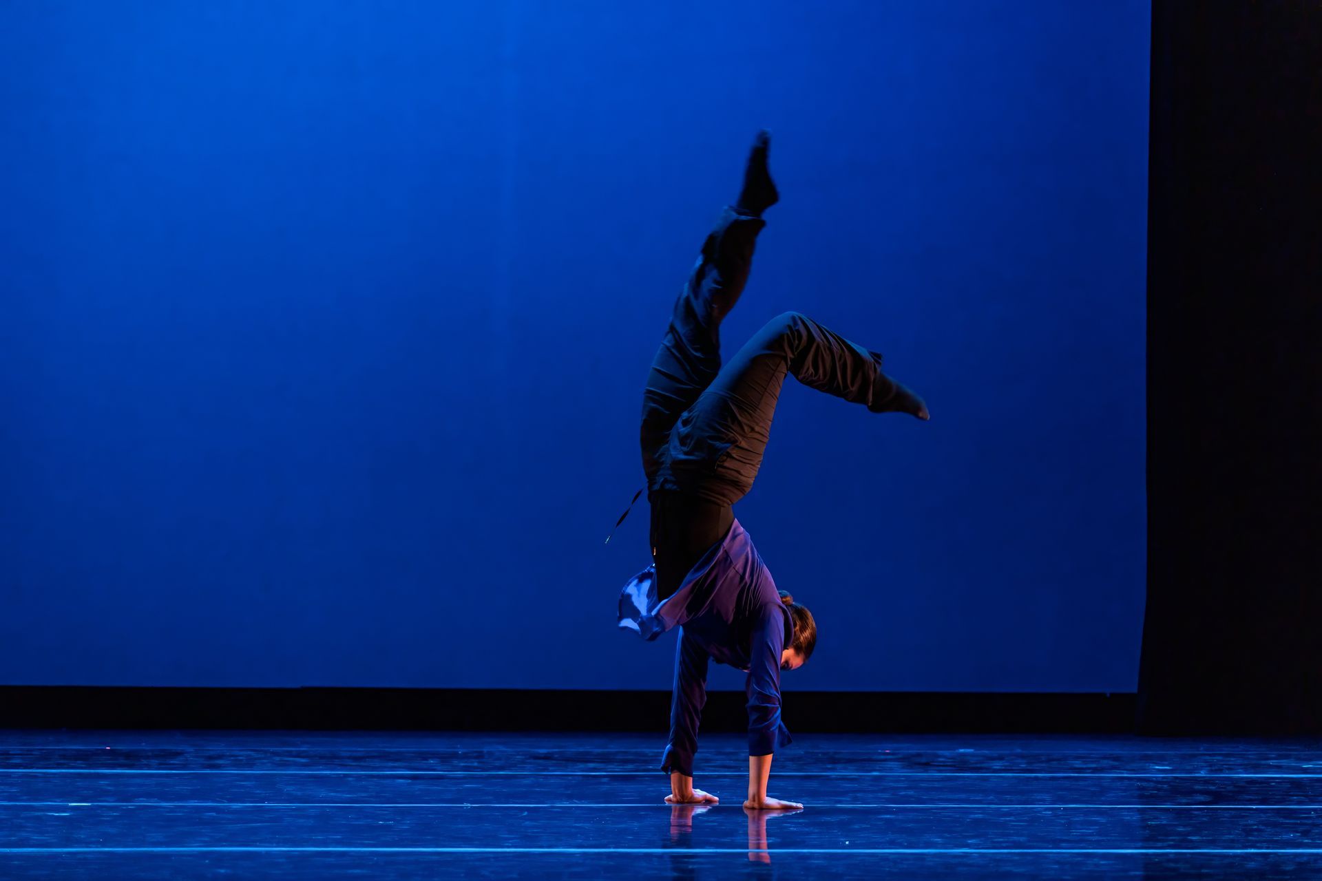 Contemporary dancer performing a handstand on a blue-lit stage with one leg raised