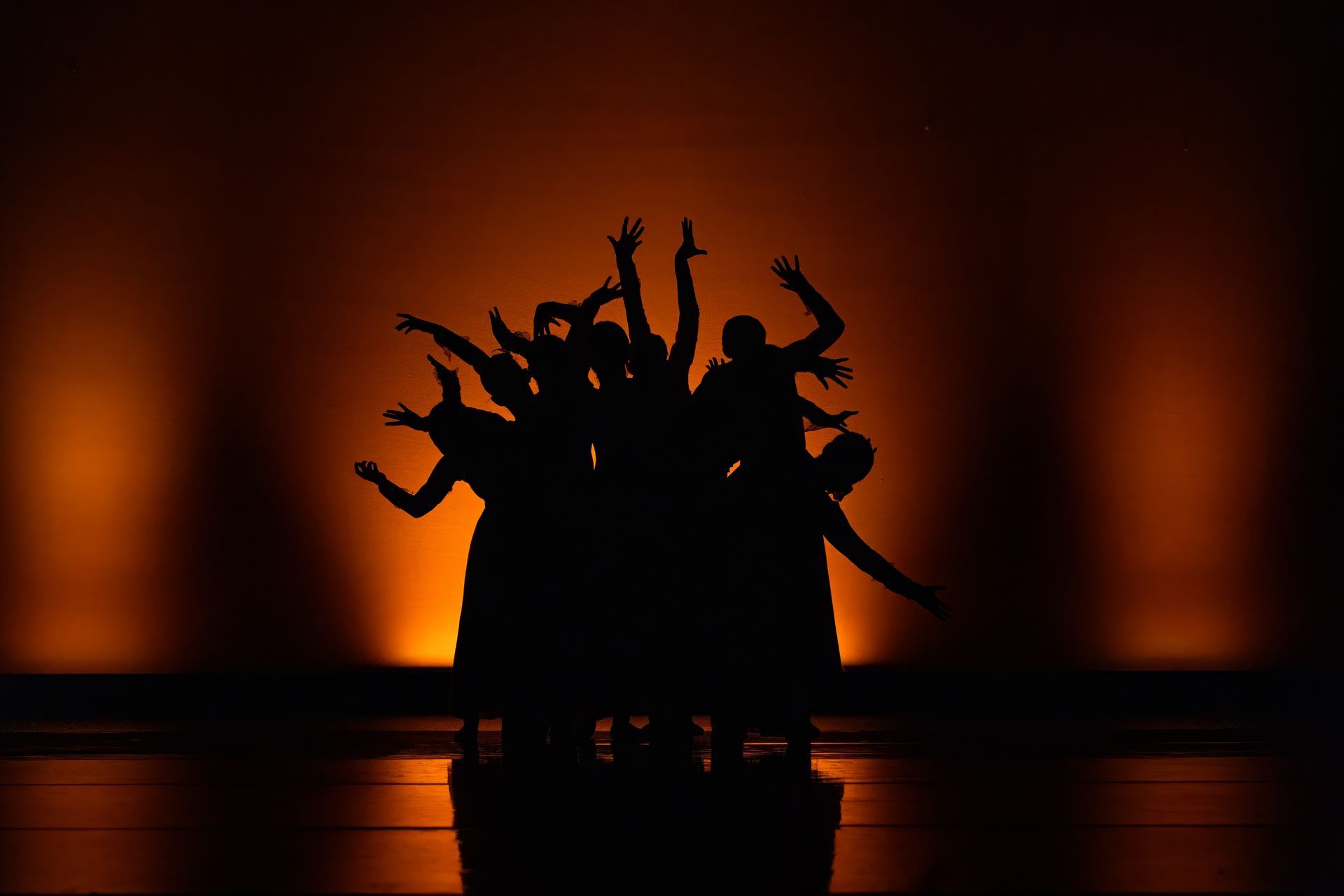 Silhouetted dancers posing on a stage against warm orange lighting