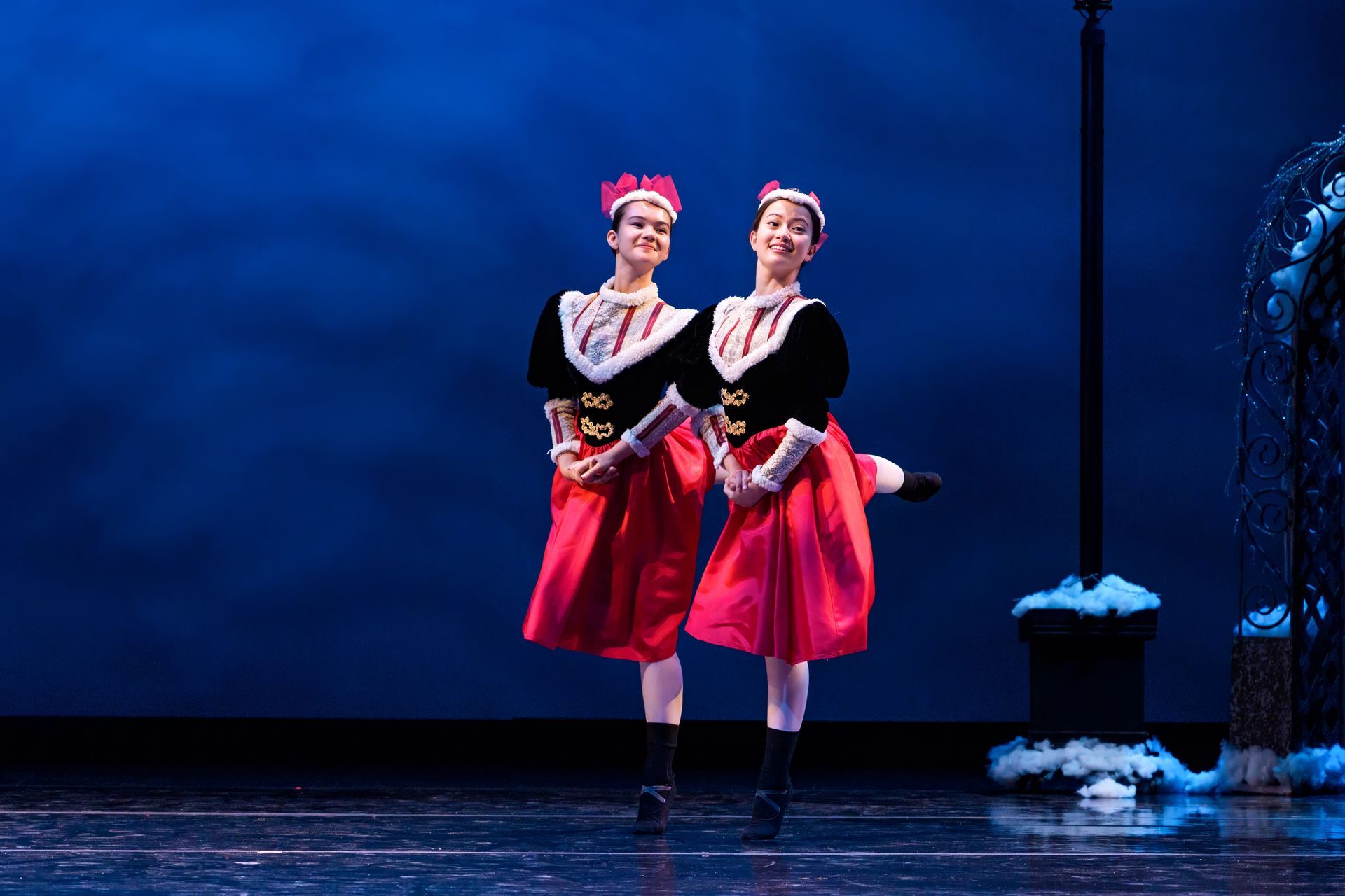 Two dancers in black and pink costumes perform on a blue-lit stage.