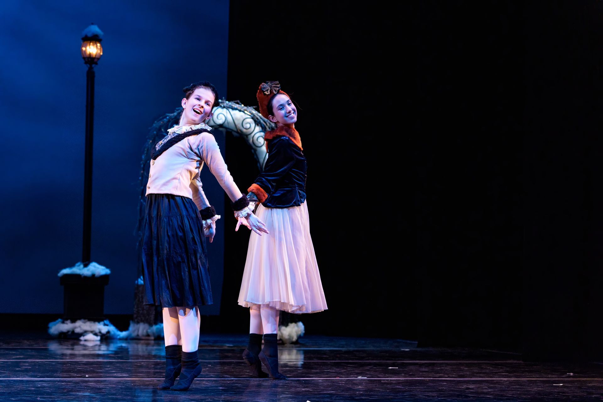 Two performers on a dark stage, leaning back-to-back under blue light, with a streetlamp prop nearby.