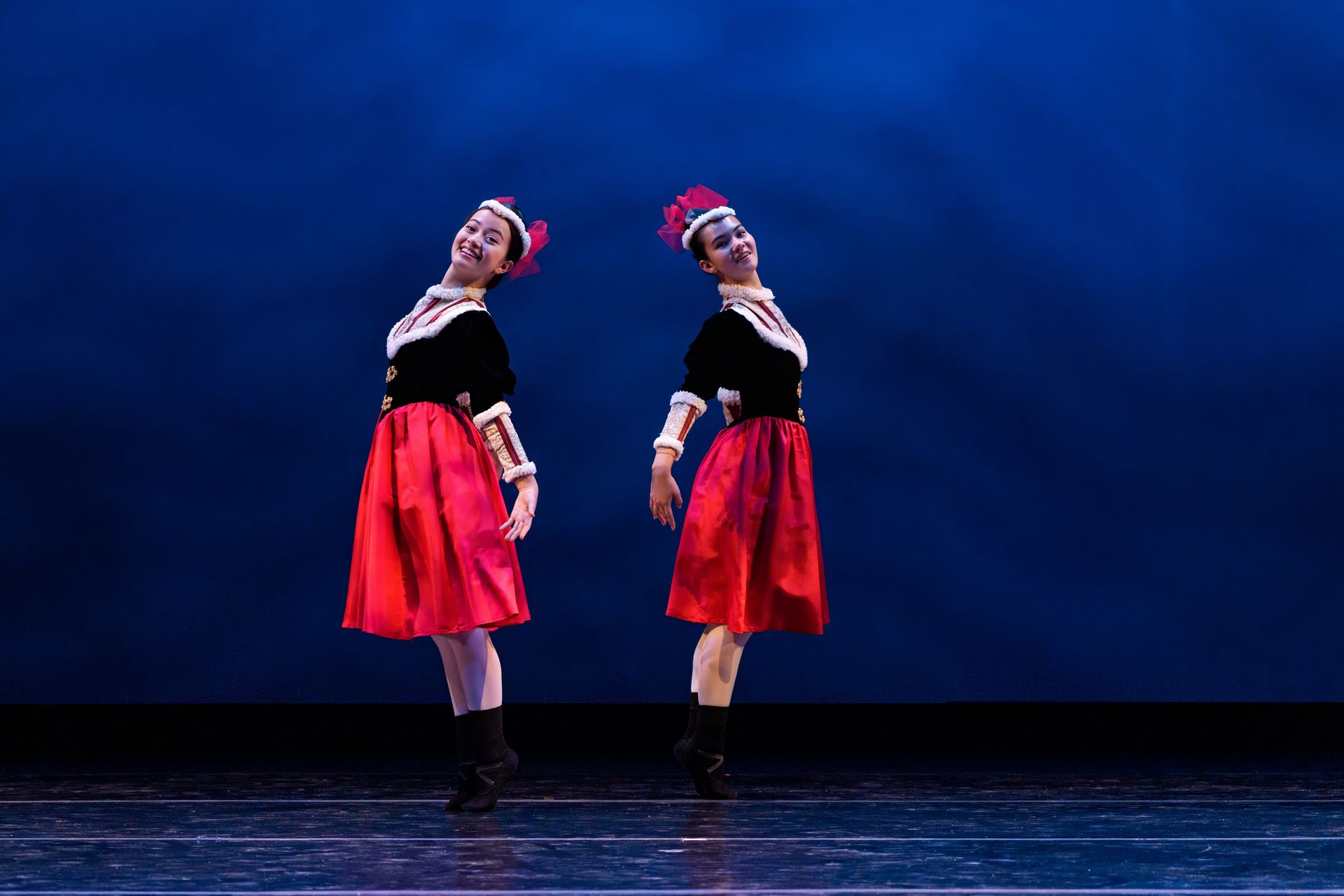Two dancers in red skirts pose back-to-back on a blue-lit stage.
