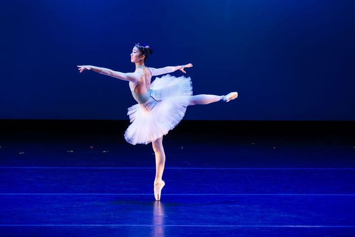 Ballet dancer in a white tutu balancing on one leg on a blue-lit stage