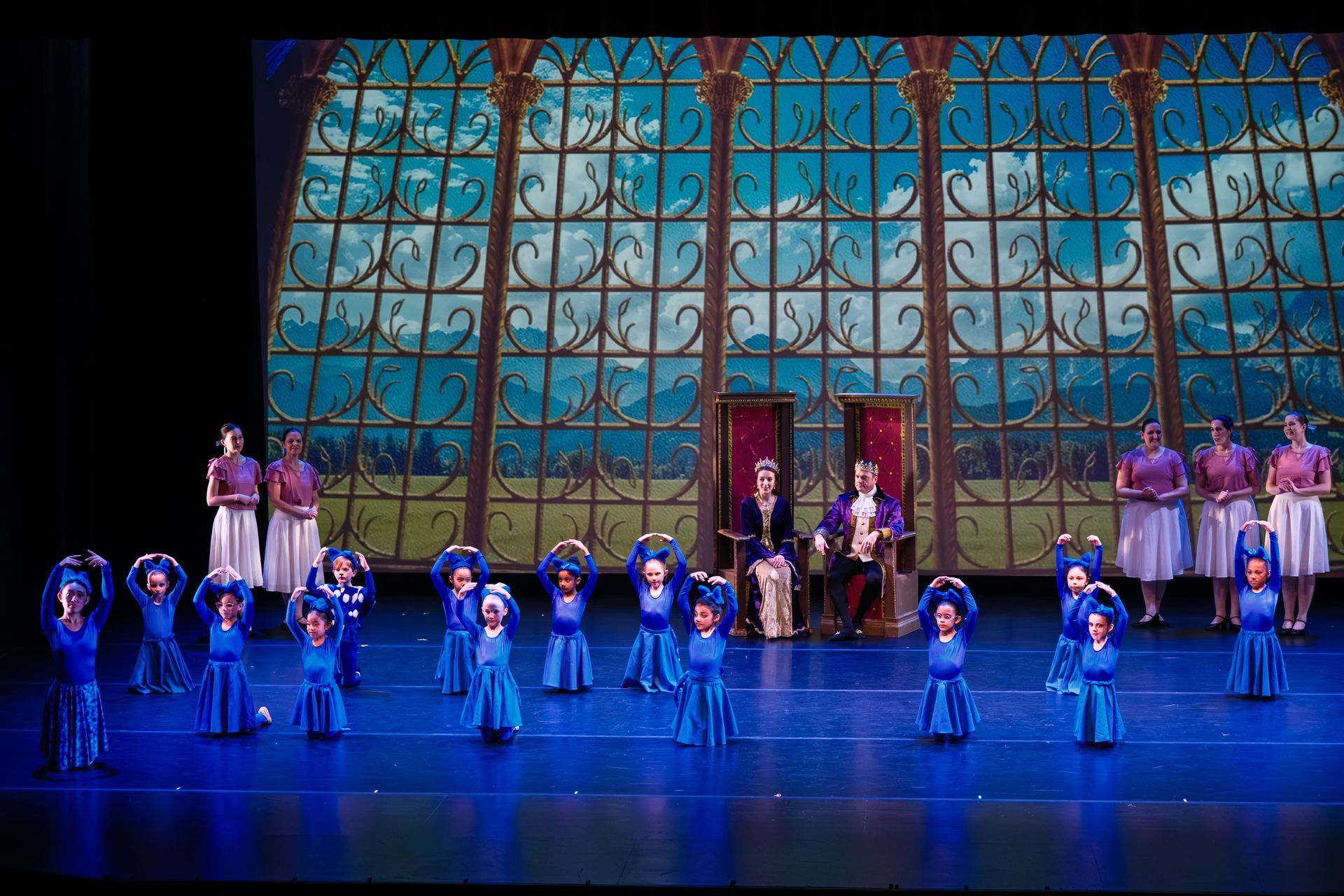 Theater stage with a large ornate backdrop and a line of performers in blue costumes under colorful lighting