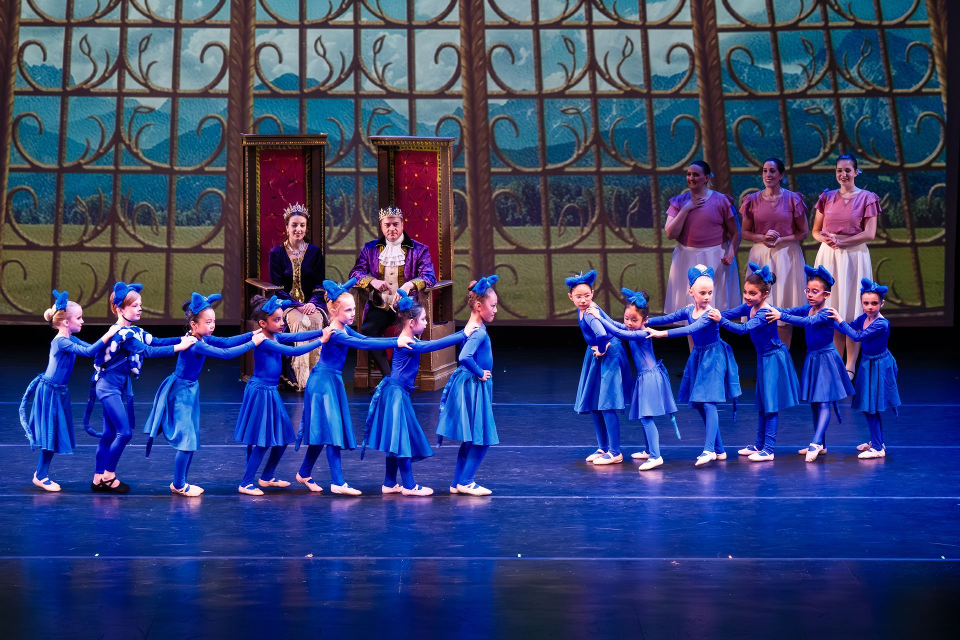 Blue-clad dancers performing on a theater stage with a colorful backdrop