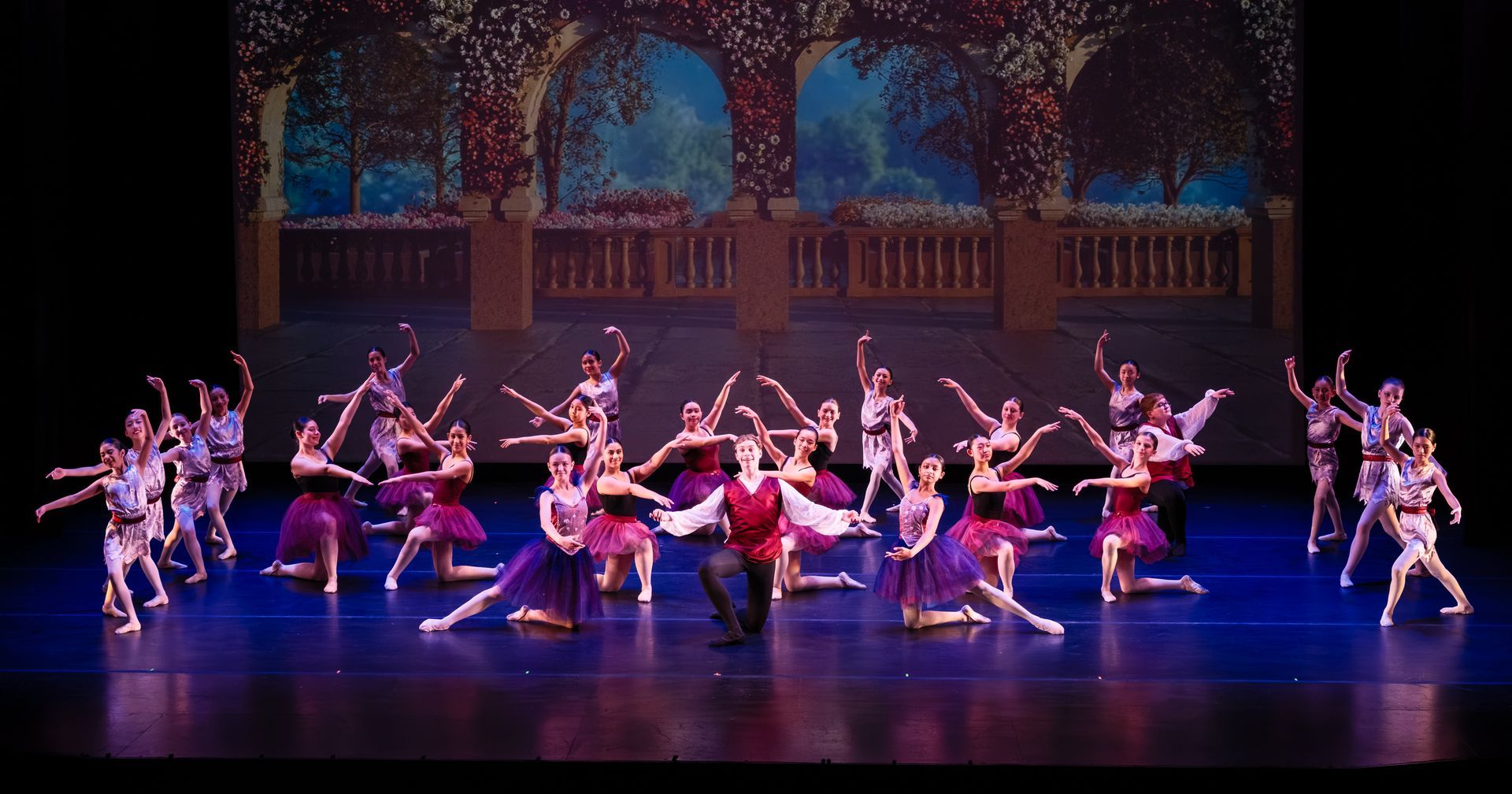 Ballet dancers performing a synchronized stage routine under purple and blue lights