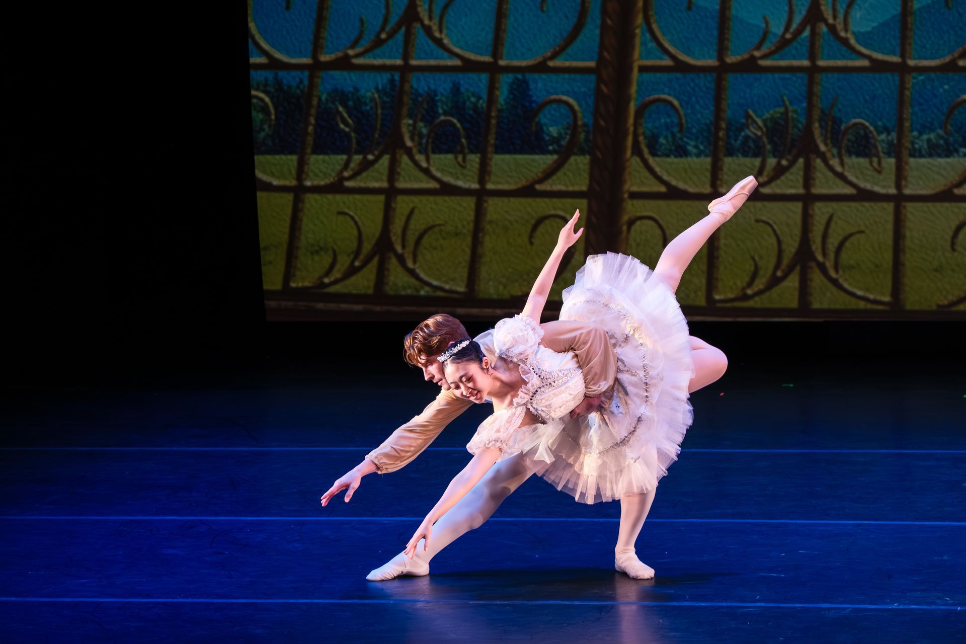 Two ballet dancers in white tutus pose in a dramatic stage performance with blue lighting