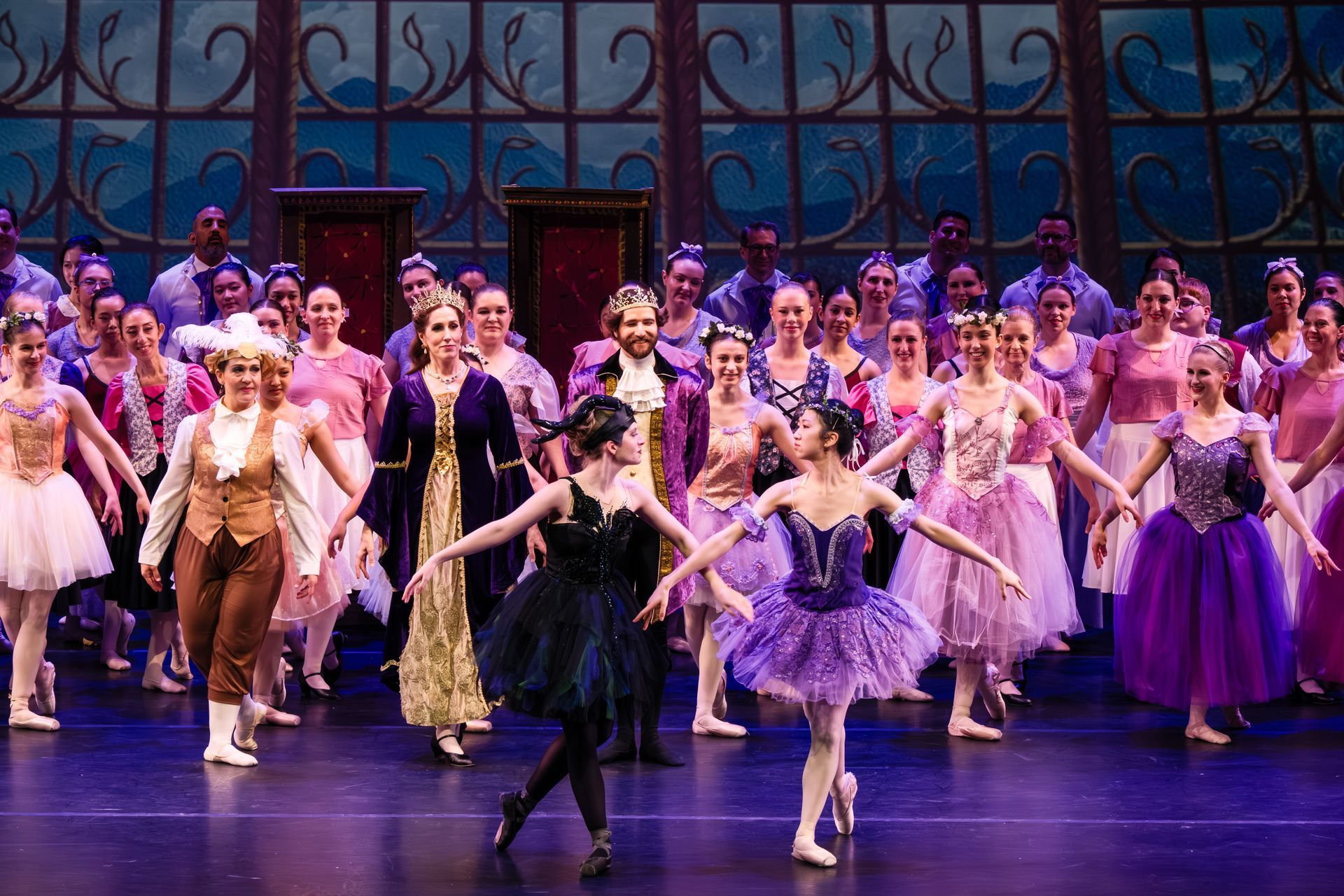 Ballet troupe in colorful costumes dancing onstage before a painted castle backdrop