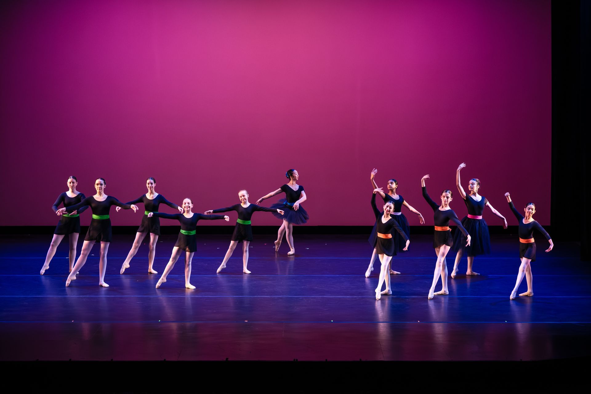 A group of dancers in black and blue costumes performing on a purple-lit stage.