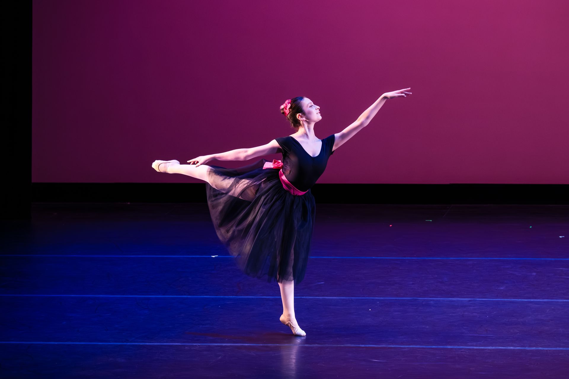 Ballet dancer in a black dress posing on stage against a pink backdrop