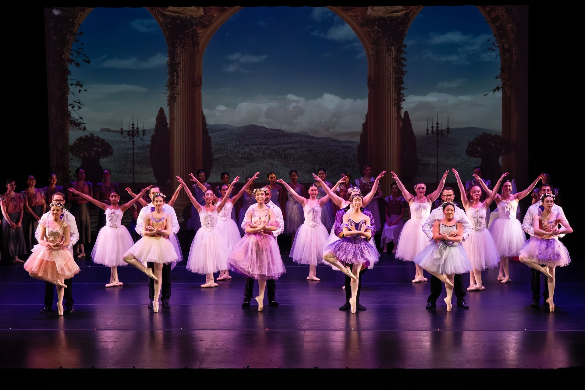Ballet dancers in white and pink costumes perform a line dance on a theater stage