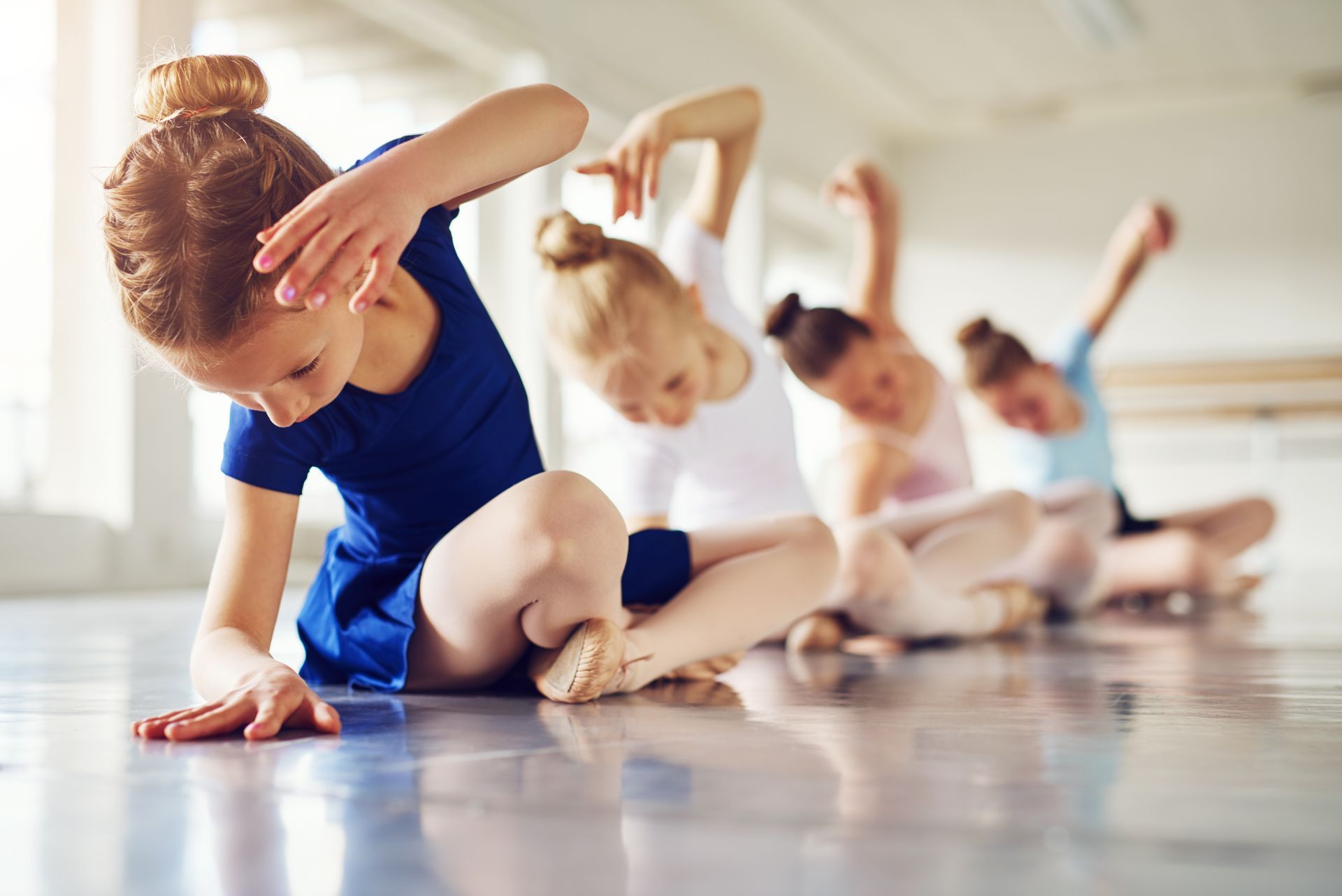 Girls bending sitting on floor in ballet class 