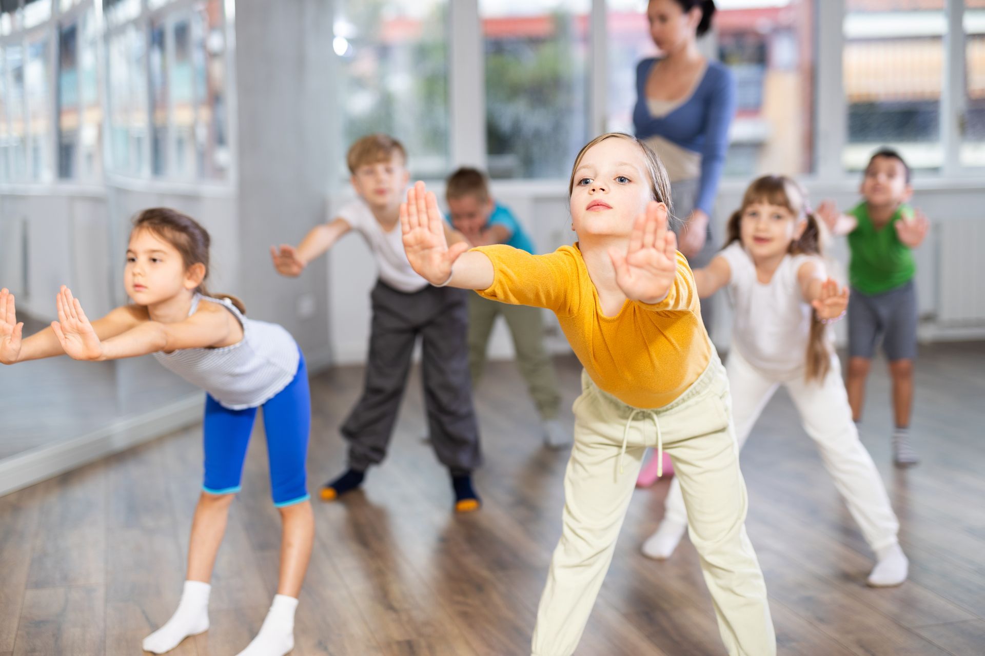 Kids in colorful activewear reach forward with arms extended in a sunlit studio during dance class. Kids in colorful activewear reach forward with arms extended in a sunlit studio during dance class.
