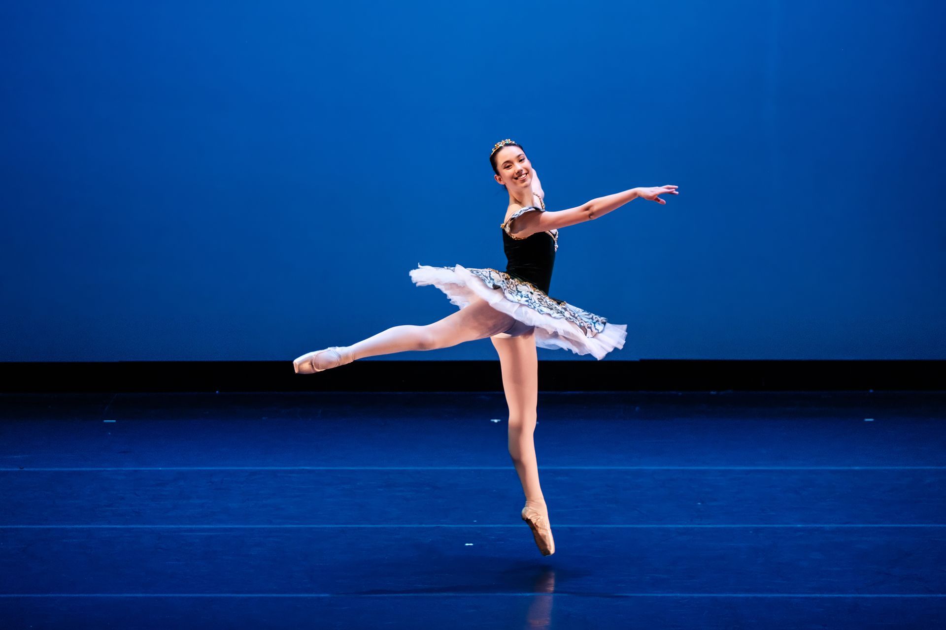 Ballet dancer in a black and silver tutu posing on stage against a blue backdrop